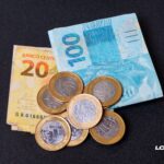 Notas de 20 e 100 reais e moedas de 1 real sobre fundo escuro, representando dívidas judiciais da União e o pagamento de precatórios — valores reconhecidos pelo governo após decisões definitivas.